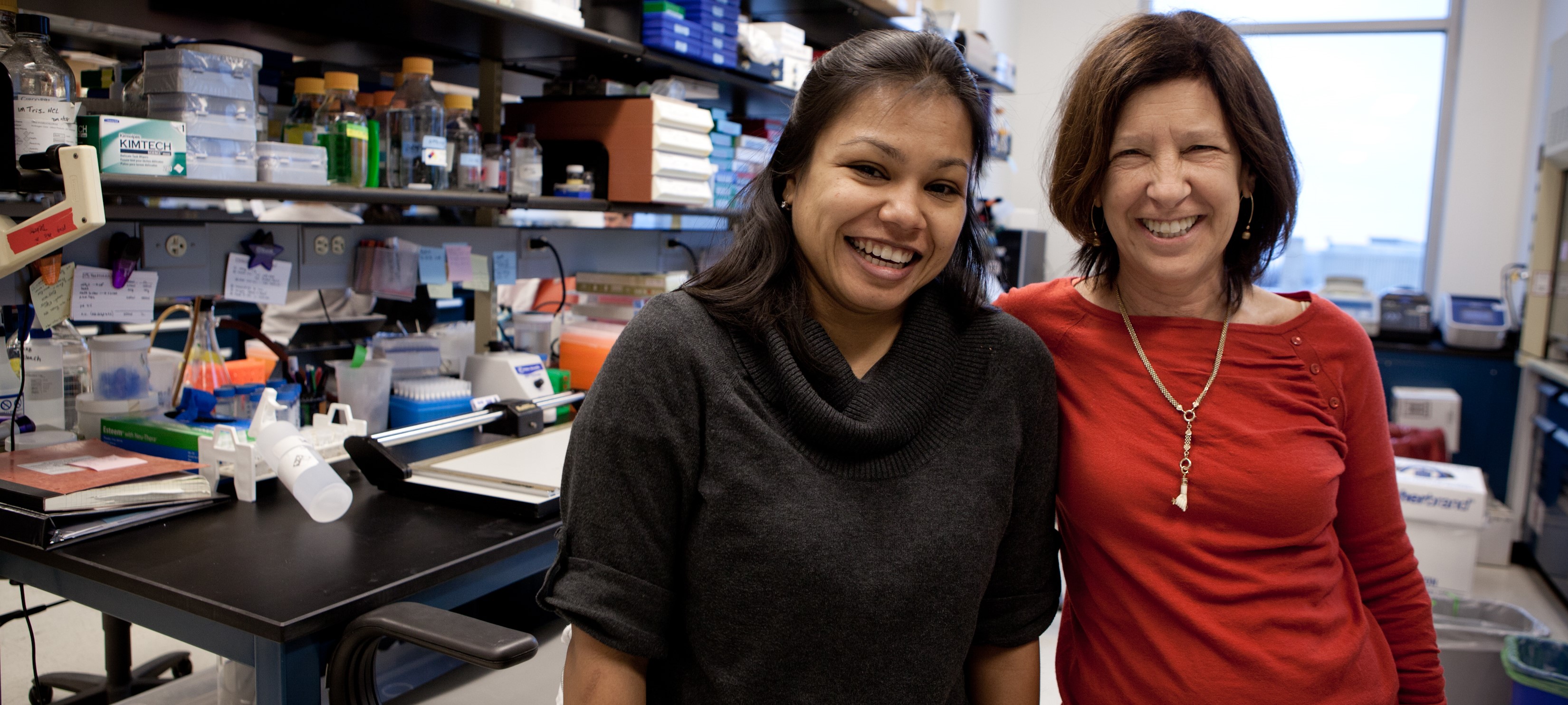 Dr. Nancy Ratner in red stands with a post-doctoral fellow in lab
