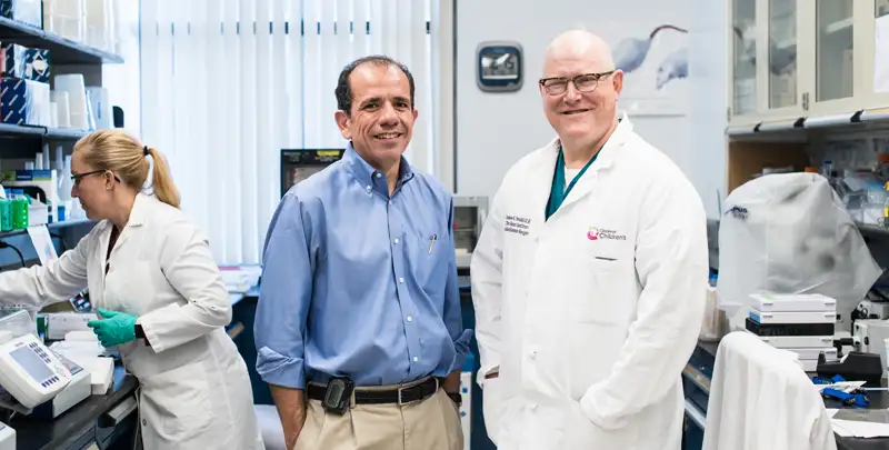 Dr. Palumbo in blue shirt stands next to Dr. Tweddell in white lab jacket