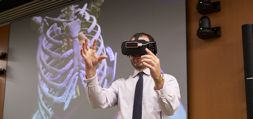 Dr. Ryan Moore wears a virtual reality headset while a 3D image of a human chest and rib cage rotates under his commands.