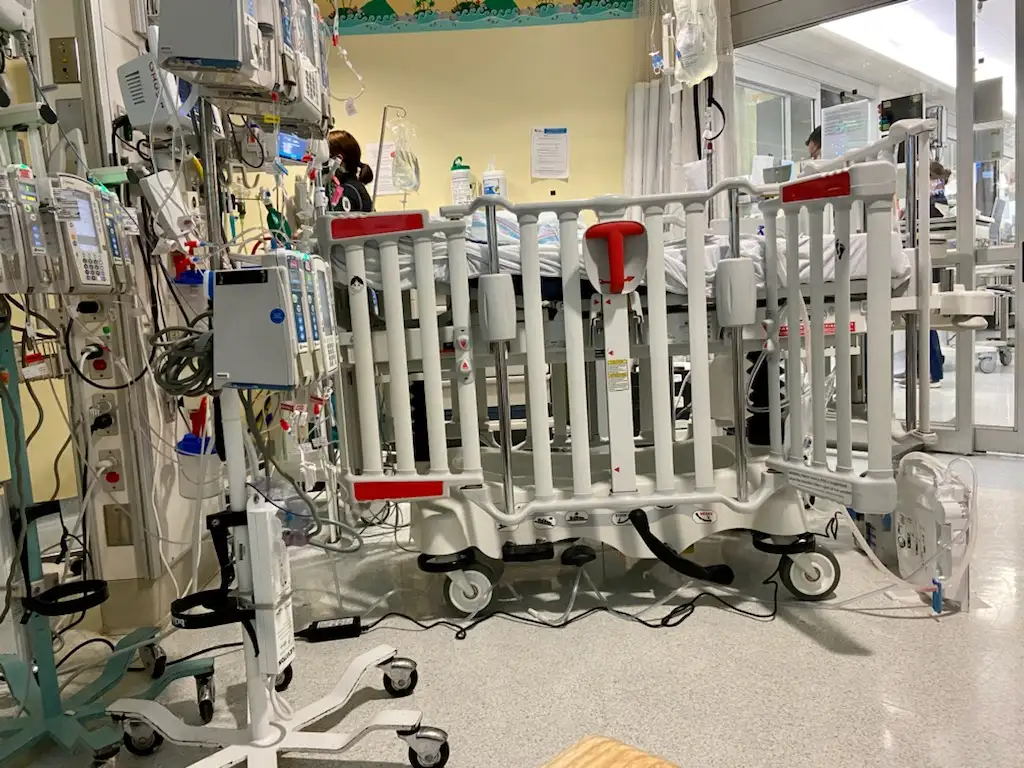 Crib in neonatal intensive care unit surrounded by monitors and equipment.