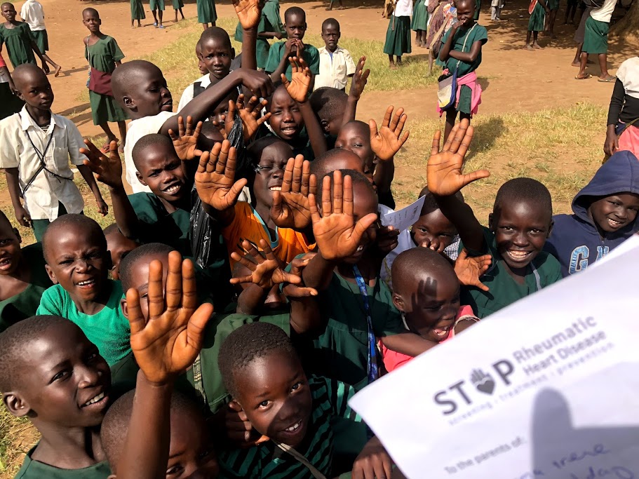 Crowd of Ugandan children, some with raised hands, lining up to participate in the GOAL study.