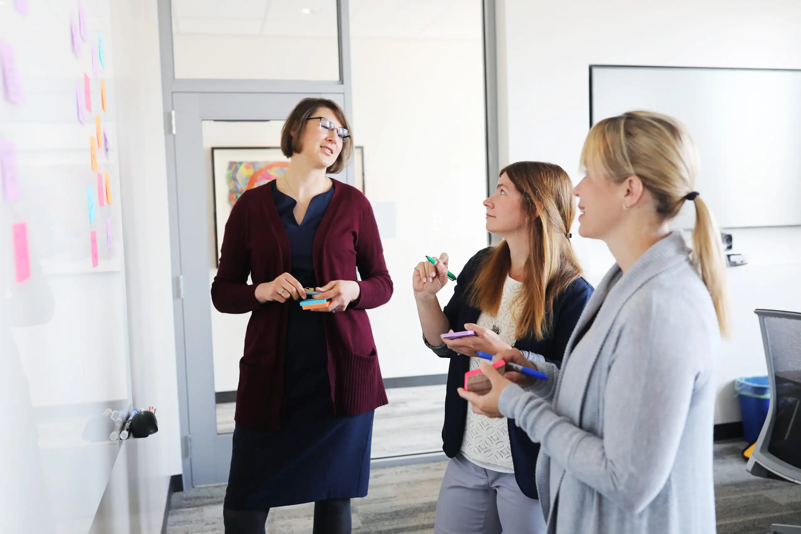 The photo depicts Sarah Beal, PhD, Mary Greiner, MD, MS, and Judith Dexheimer, PhD with a white board and post it notes, brainstorming ways to address the issue of data sharing for children in the child protective custody.