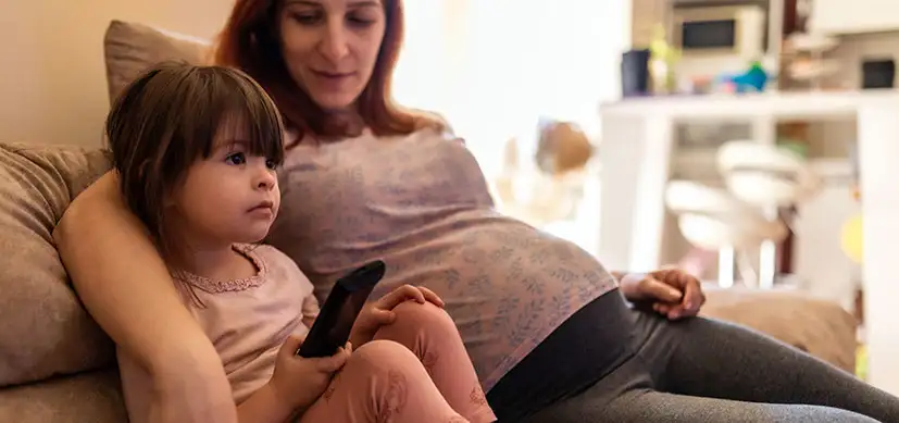 Pregnant mother and child relax on a couch with a remote control