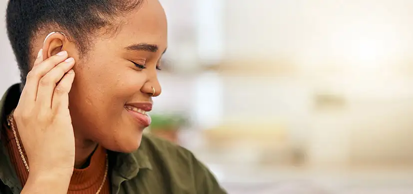 Black female touching her hearing aid and smiling